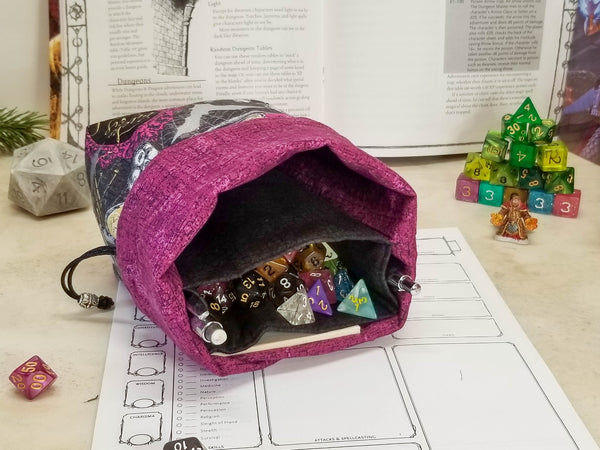 Halloween potions dice bag. Halloween print in black, metallic silver and purple with pops of gold. bag folded down to show purple lining wit black pockets