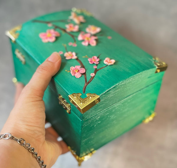 Cherry blossom chest in a shimmery mint green with 3D cherry blossoms and brass hardware.  In hand for scale