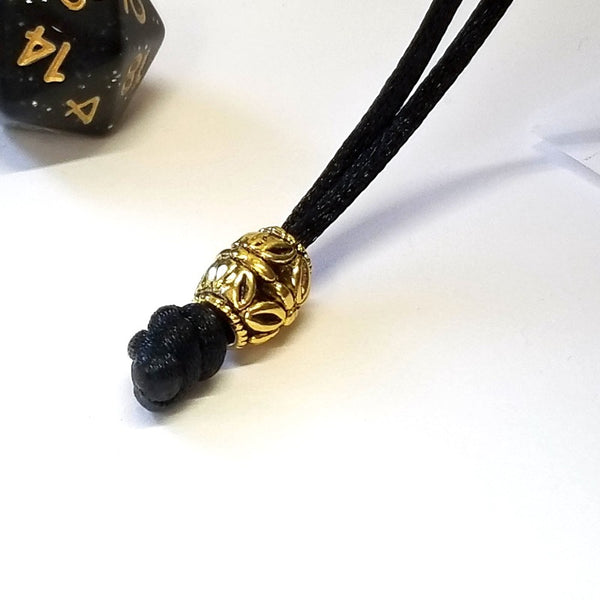 Closeup of a gold bead and terminal knot used on the dice bag.