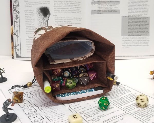 Dungeon map dice bag folded open to show brown crackle lining with storage pockets. Lying on its side to show spellbook and dice inside