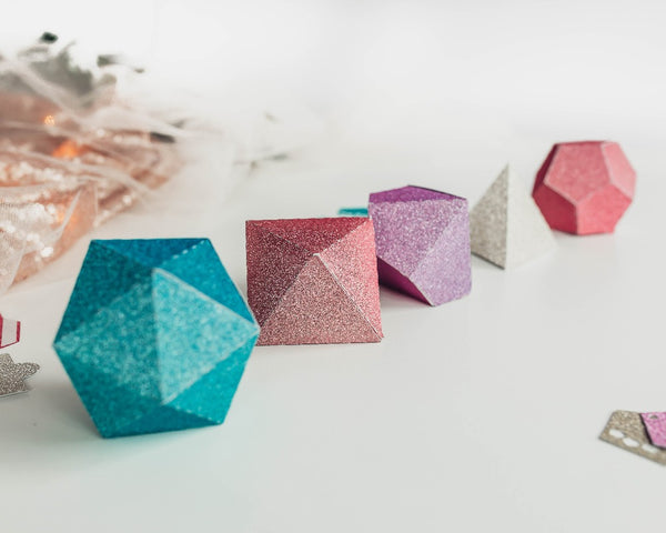Pastel glitter paper dice favor boxes lined up in a row. 